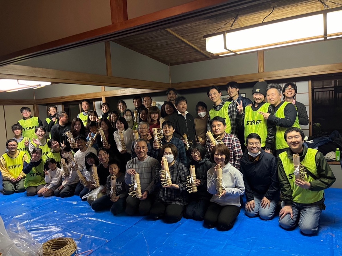 松明づくりワークショップの集合写真。参加者と学生スタッフが手づくりの小松明を掲げる